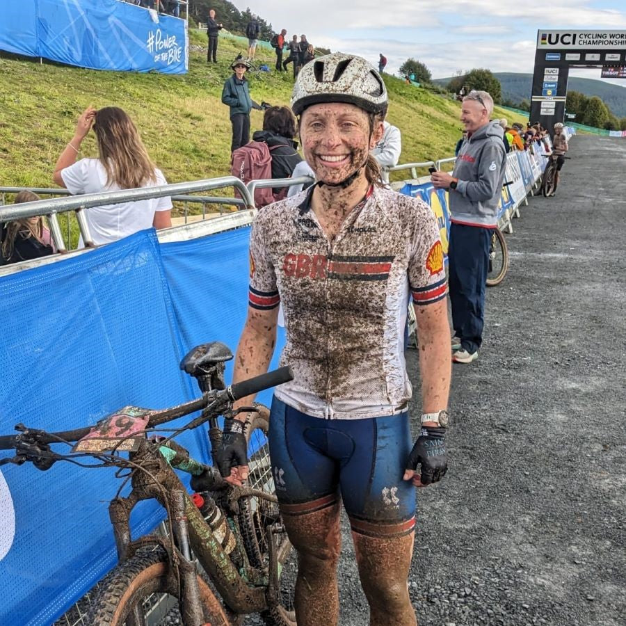 muddy but happy cyclist stands by her bike at the end of a gravel race