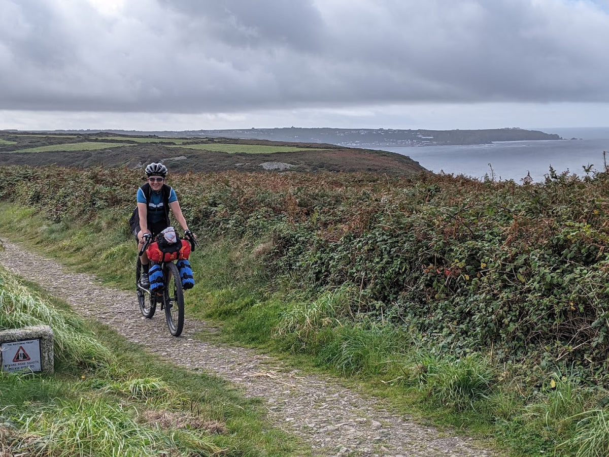 Cyclist riding down a rocky road in the countryside with green hilly landscape in the background