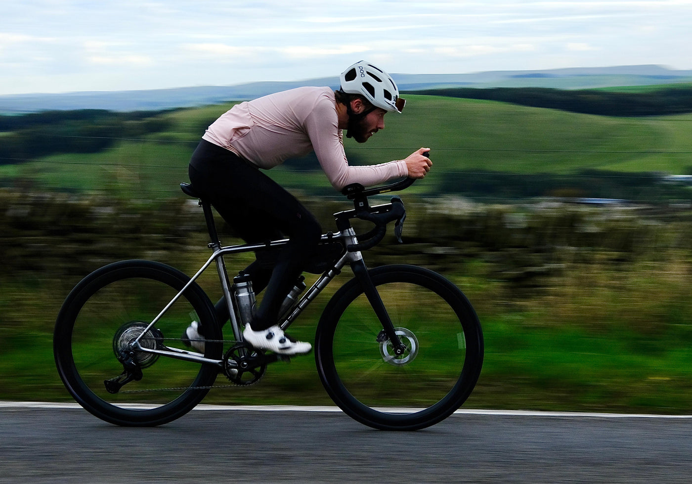 A cyclist on a titanium bike rides past fields.
