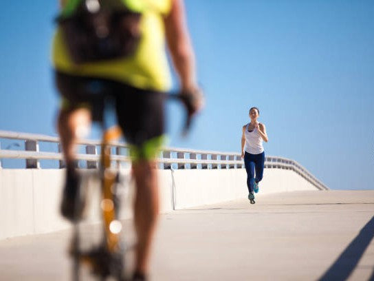 A woman running towards a blurred cyclist on a bike. They are on a bridge with a blue sky.