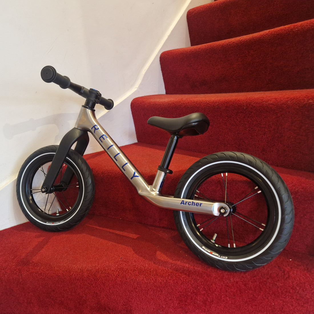 Children's balance bike on red stairs with 'REILLY' branding
