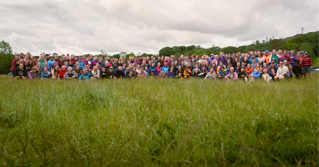 Large group of people standing in a grassy field with trees and cloudy sky in the background