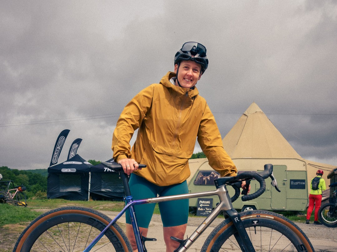 Person in yellow jacket and helmet standing next to a bicycle with a cloudy sky and tents in the background