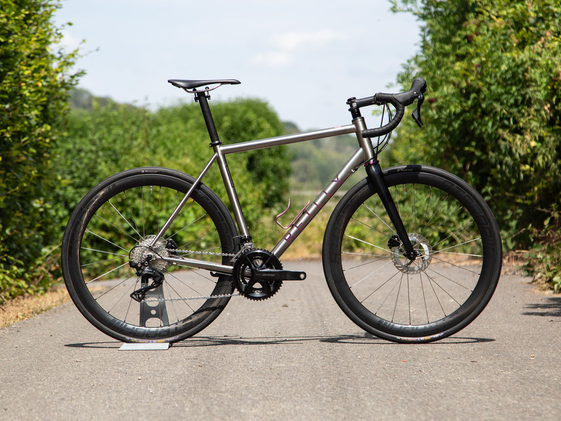 A titanium road bike on tarmac with green either side.