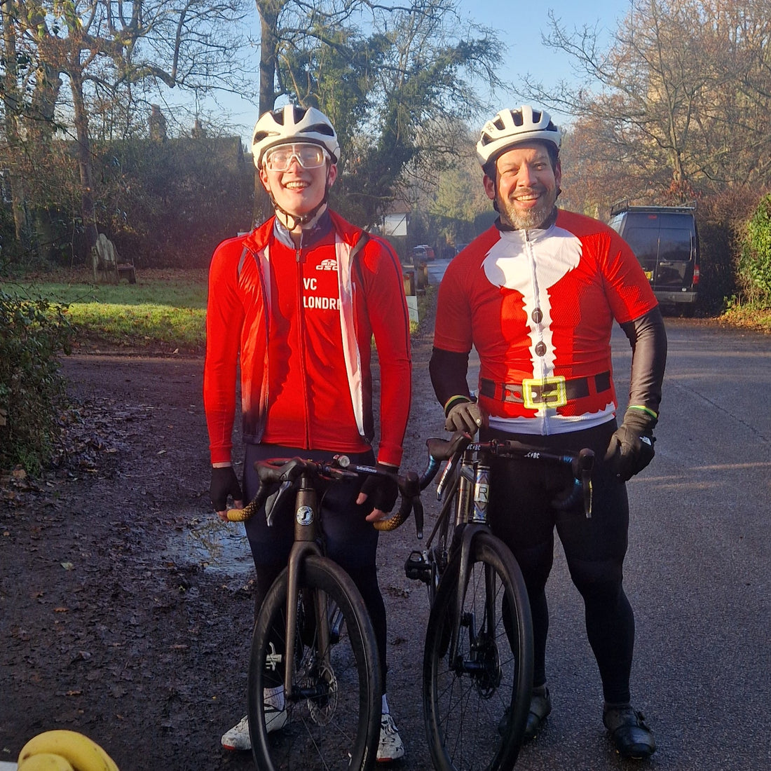 Two cyclists in red jerseys with festive designs standing on a road.