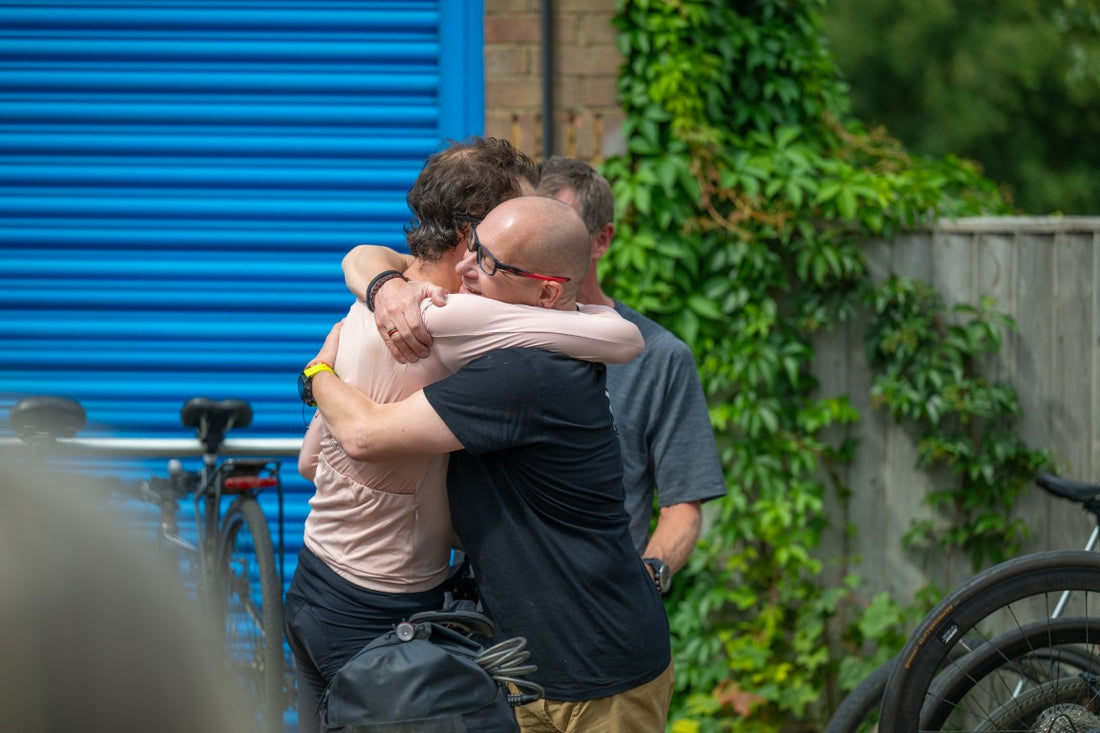 Two men hugging outdoors with a blue storage unit and greenery in the background
