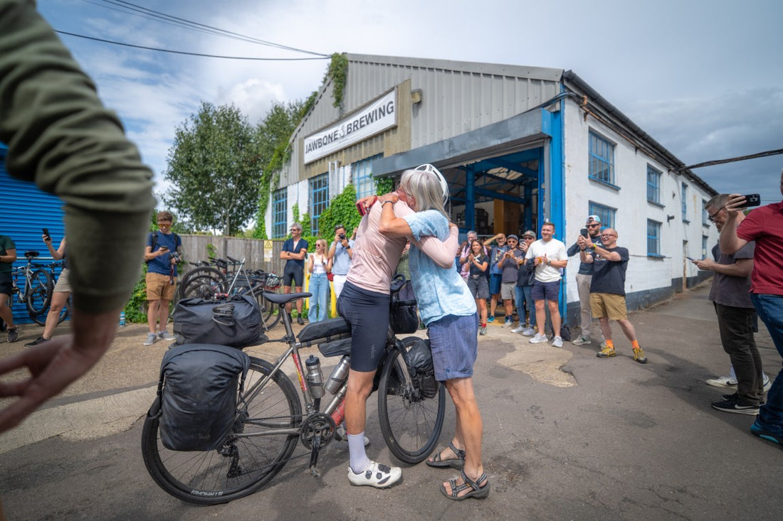 Two people embracing outside a brewery with onlookers and bicycles.