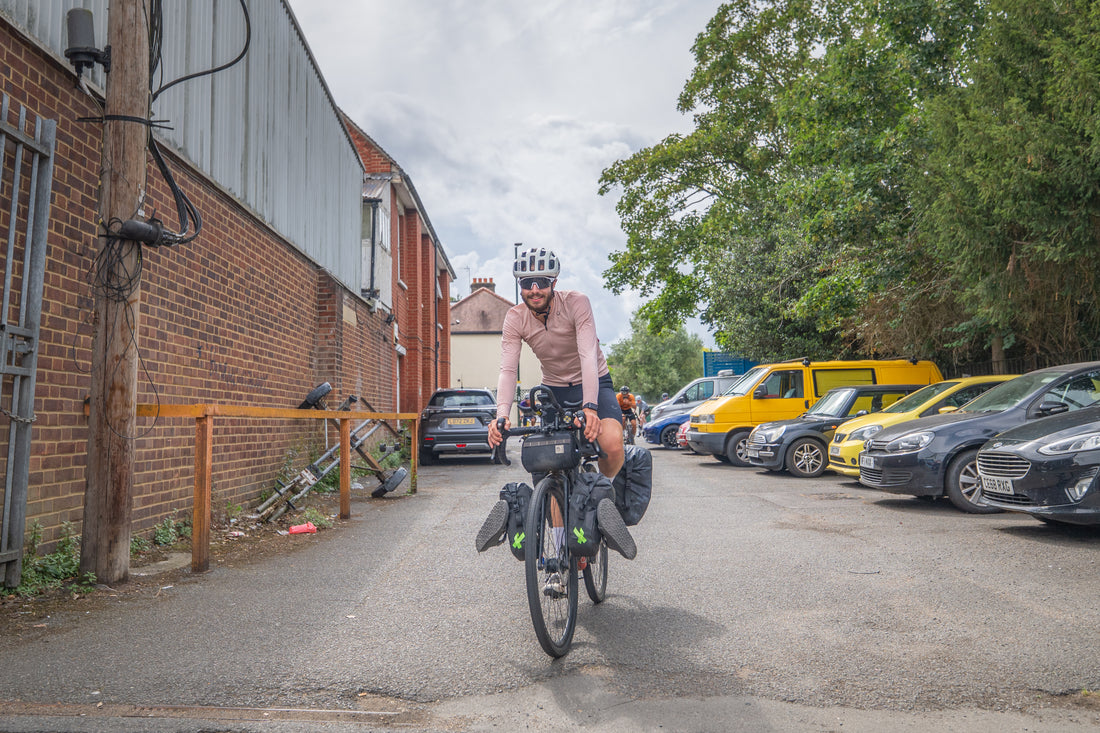 Person riding a bicycle on a street with parked cars and buildings in the background