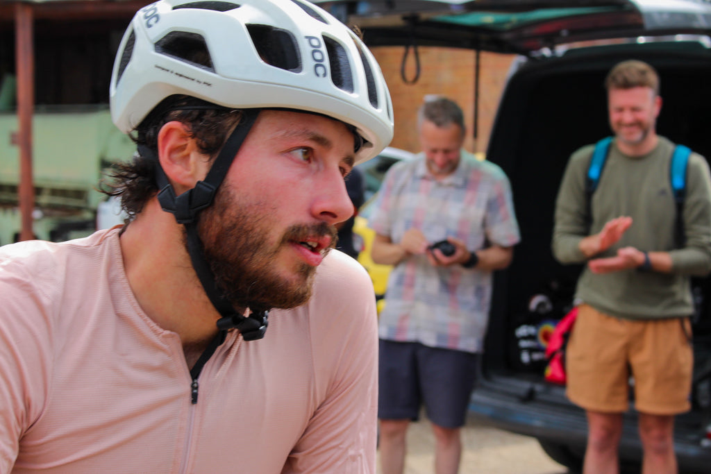 Cyclist wearing a helmet with another man in the background near a vehicle