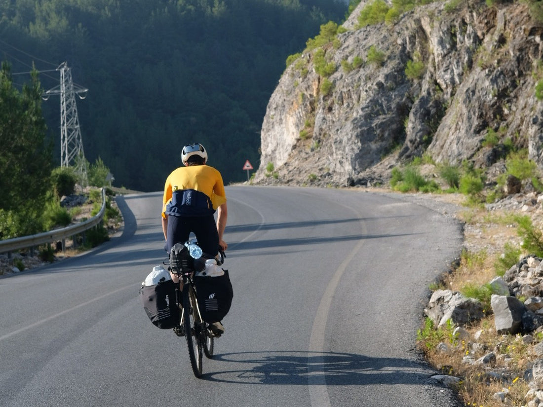 A cyclist rides along a road with dramatic mountain in the background.