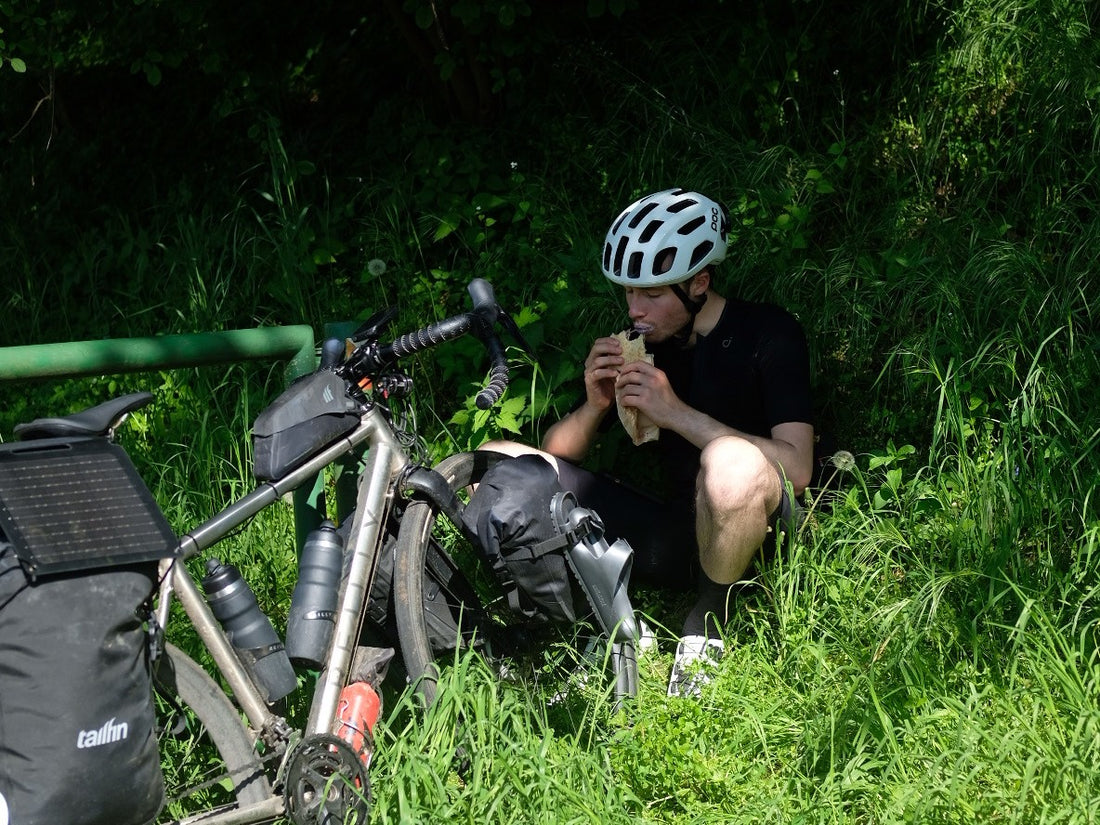 A cyclist eats a baguette after a long day of cycling