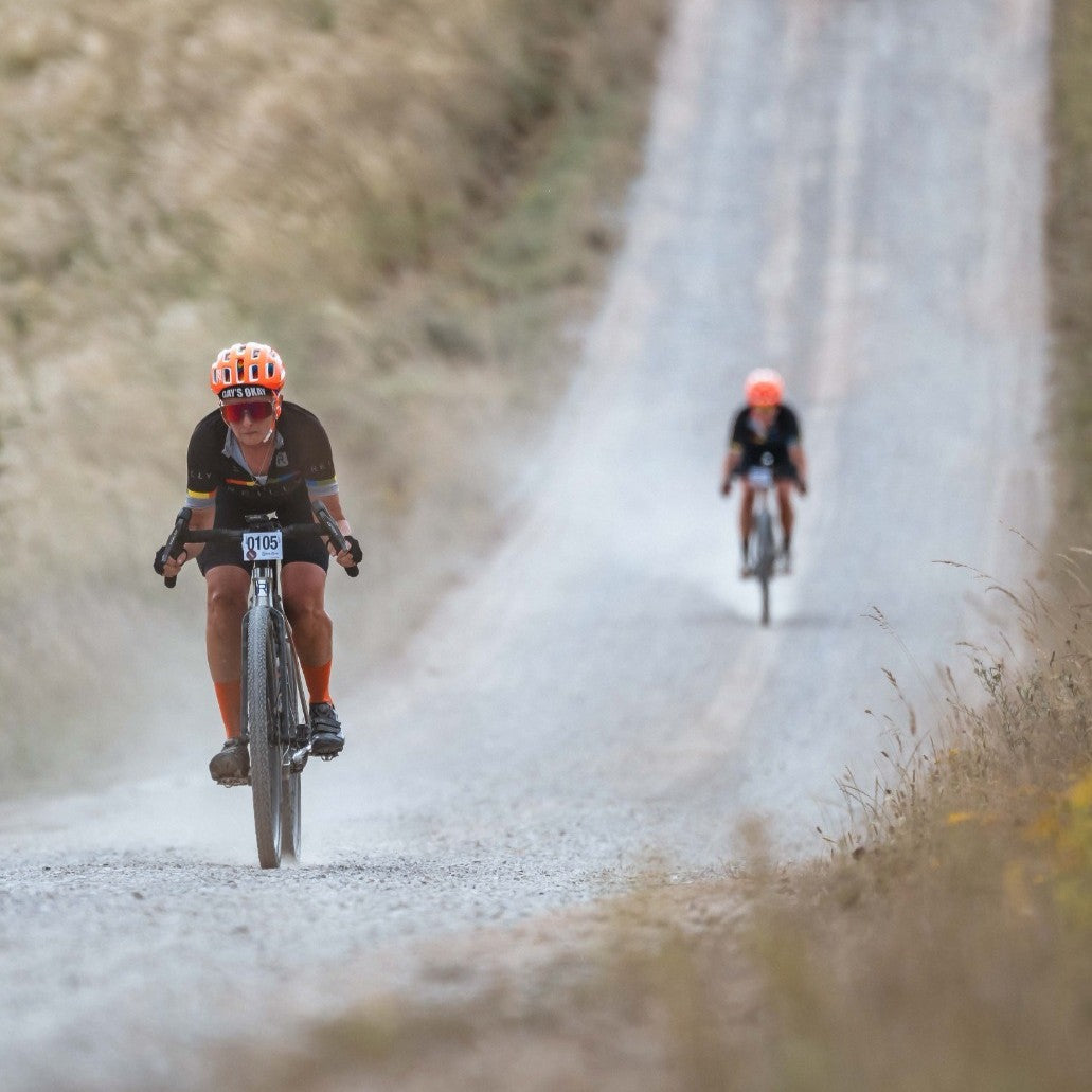 Two cyclists on a gravel road with one in focus and the other blurred.