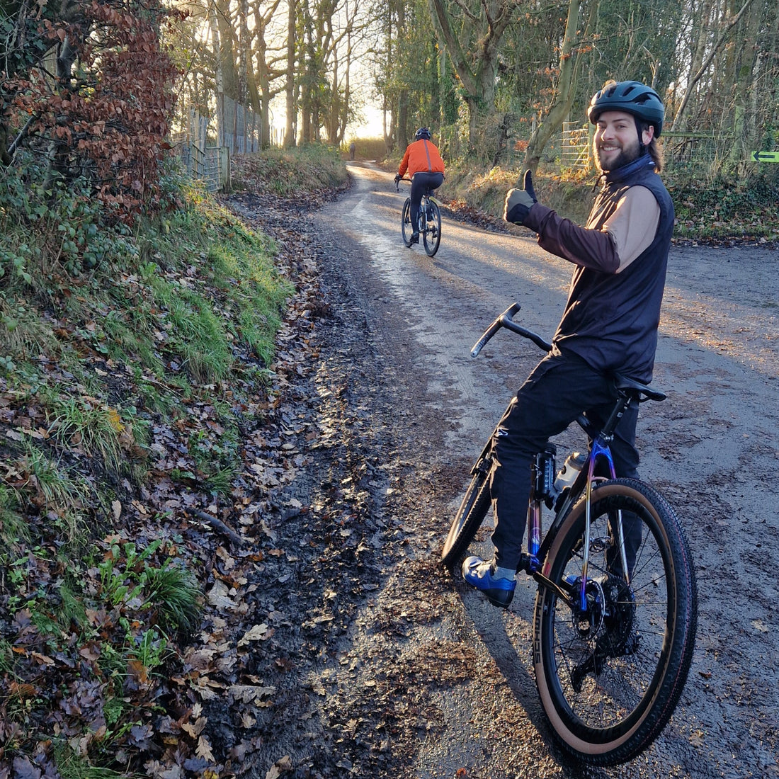 Two cyclists on a rural road with trees and foliage on either side.