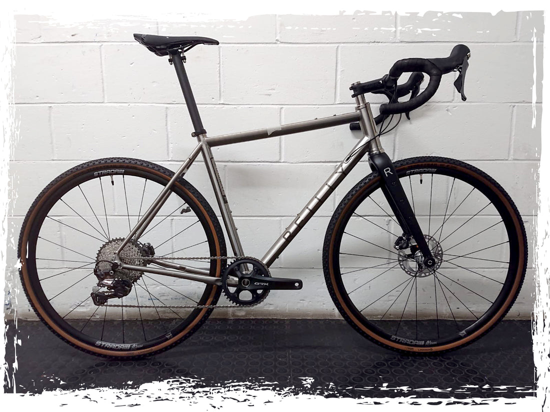 silver custom Reilly titanium bike photographed in front of white wall.