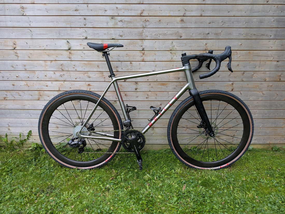 custom Reilly titanium bicycle leaning against a wooden wall on grass