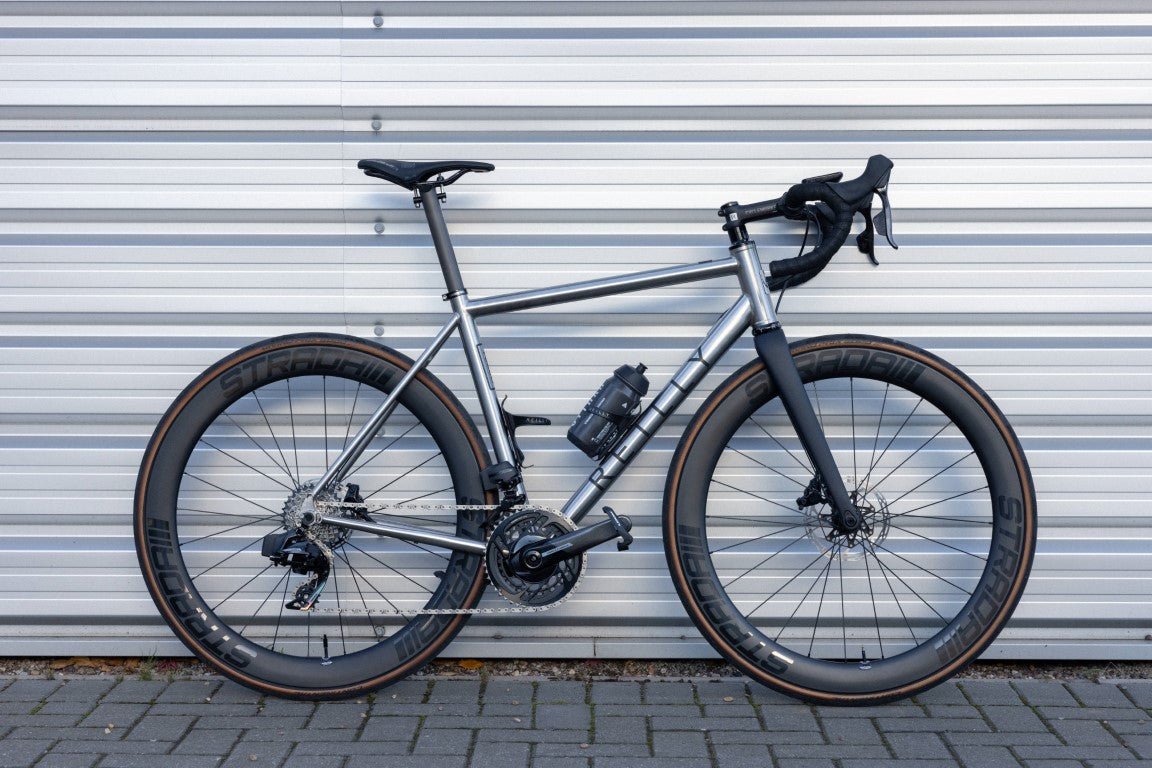 T325 D road bike in brushed titaniumm with Strada wheelset against a metal door.