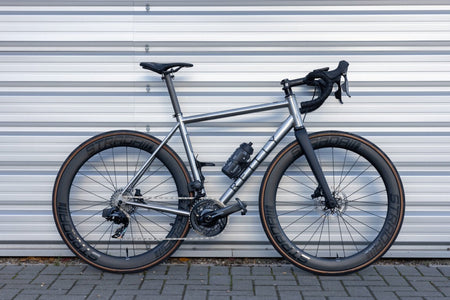 T325 D road bike in brushed titaniumm with Strada wheelset against a metal door.
