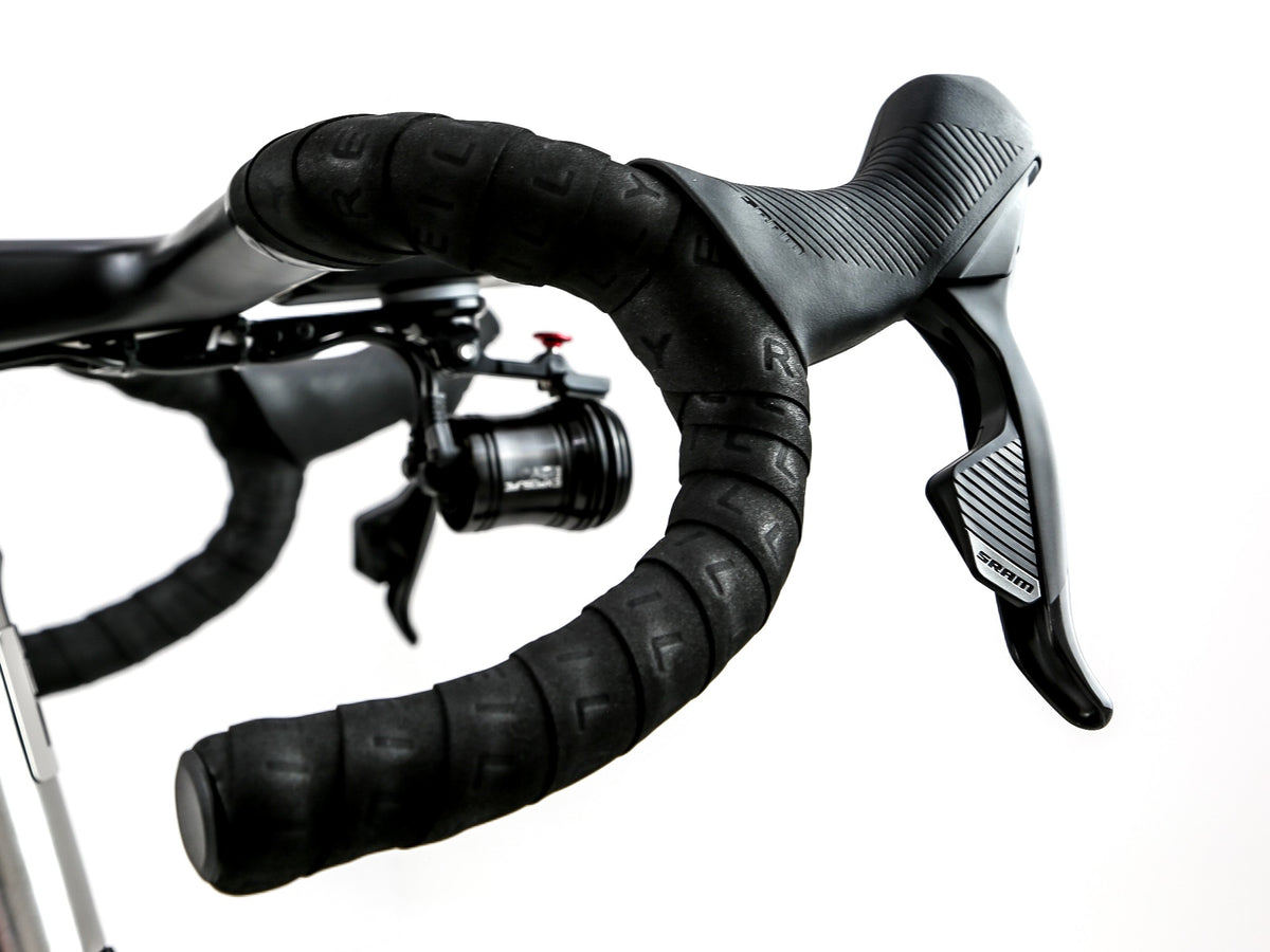 Close-up of black drop handlebar tape and a black Shimano road bike shifter lever on a white background.