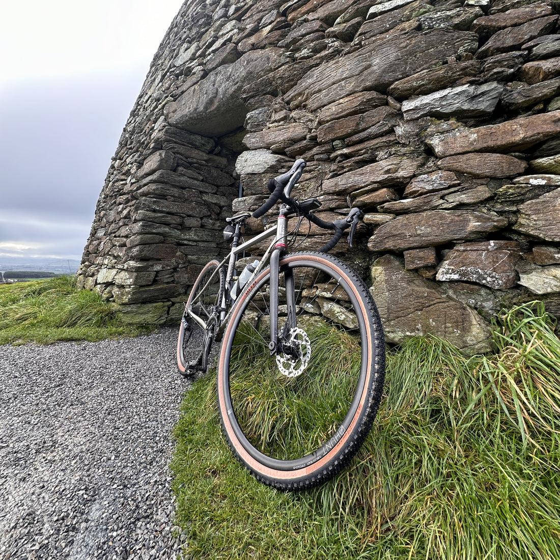 a bike stood on grass, in front of a stone wall with a foggy sky in the background