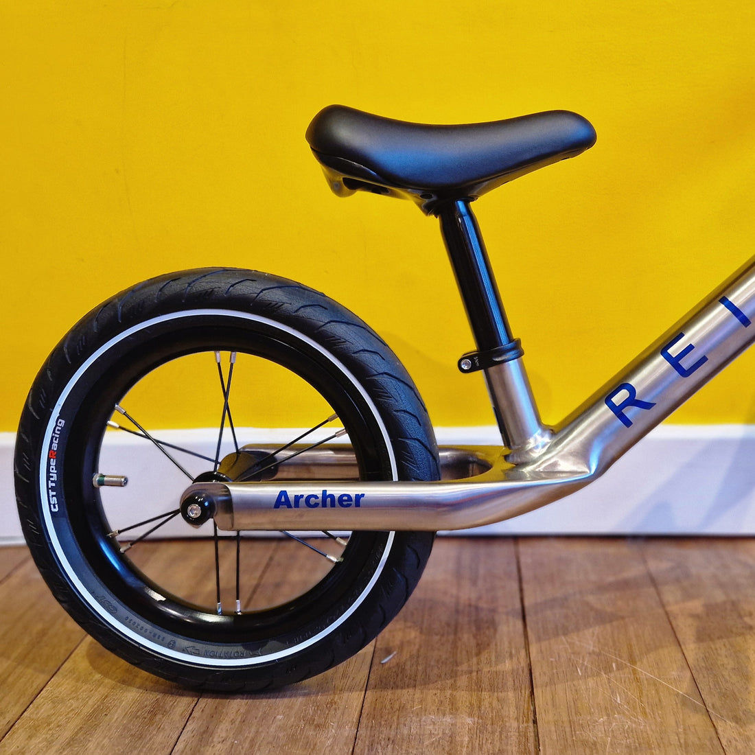Balance bike with black tire and silver frame against a yellow wall