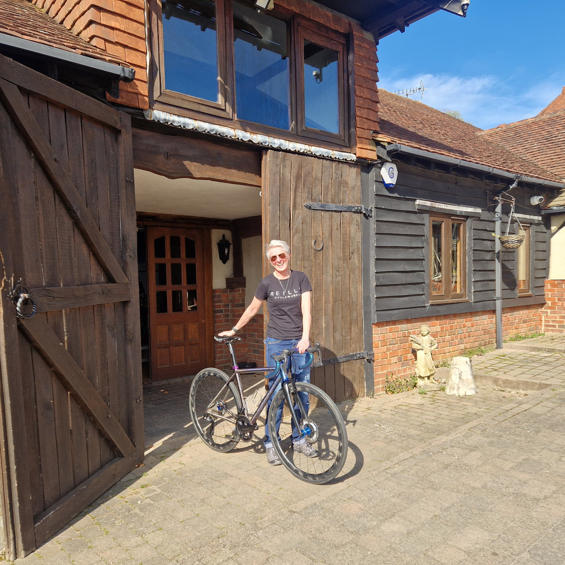 Person standing with a bicycle in front of a wooden building