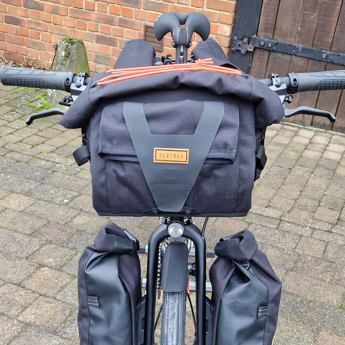 Bicycle with a gray bag attached to the handlebars on a brick pavement.