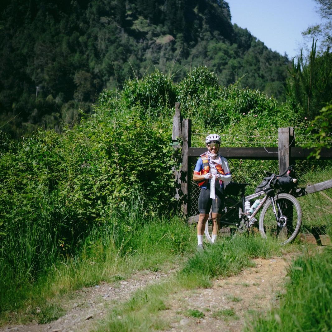 A cyclist by a stile stands by her bike.