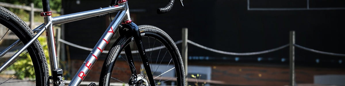 Close-up of a silver mountain bike frame with red and black 'DEAD' branding, set against a dark outdoor background with a rope barrier.