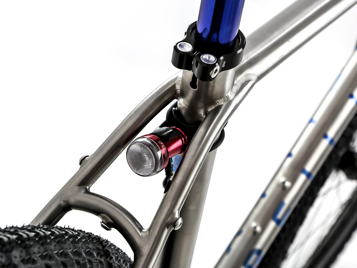 Close-up of a bicycle frame with a red and silver front light attached near the head tube, a blue seat post, and part of a black tire on a white background.