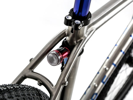 Close-up of a bicycle frame with a red and silver front light attached near the head tube, a blue seat post, and part of a black tire on a white background.