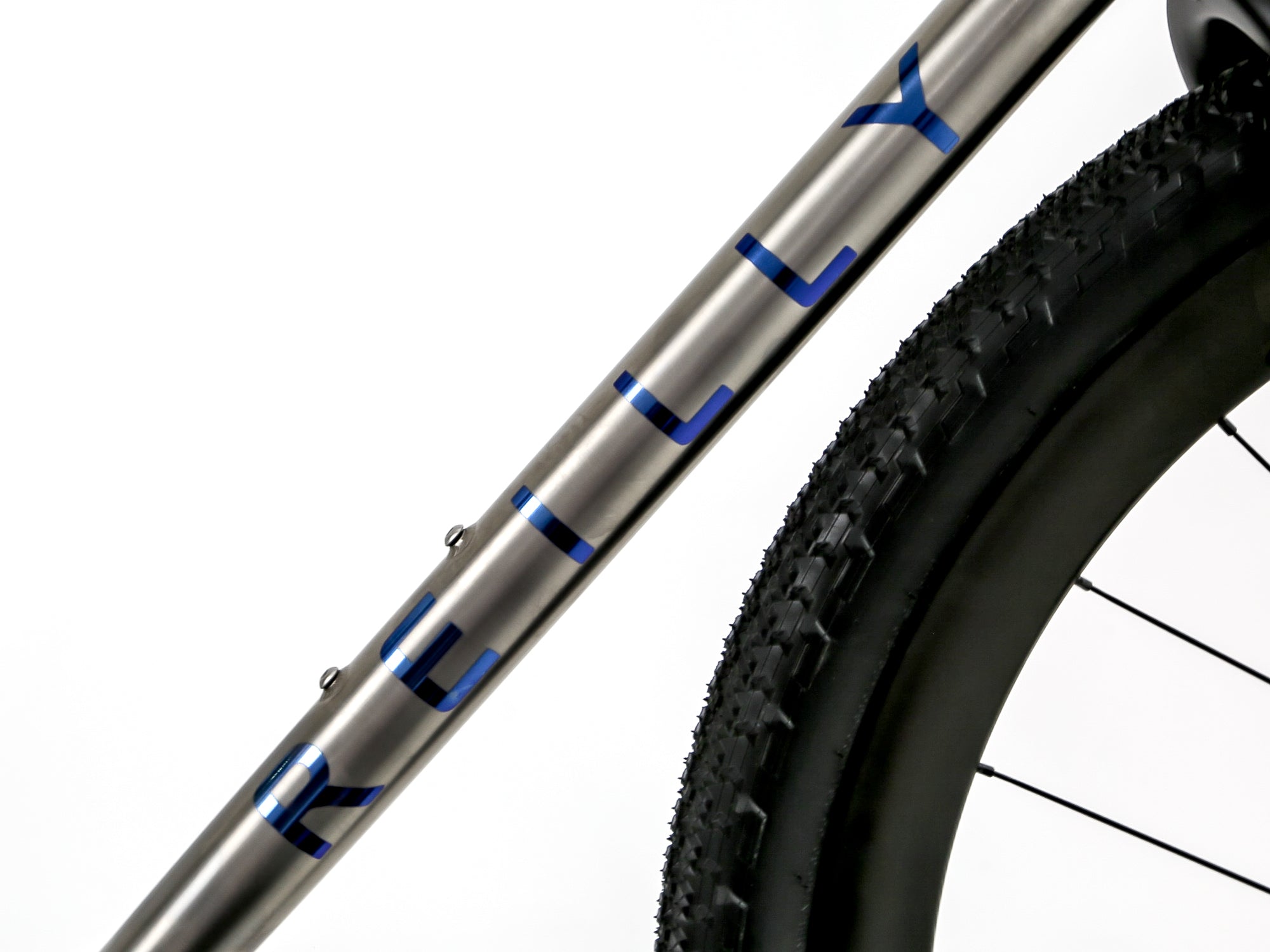 Close-up of a bicycle frame tube with the brand name 'KILLY' in blue on a metallic silver finish, alongside a black tire and wheel against a white background.