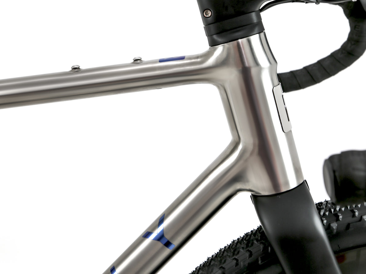 Close-up of a metallic silver bicycle frame with black handlebar tape and a black tire, shown against a white background.