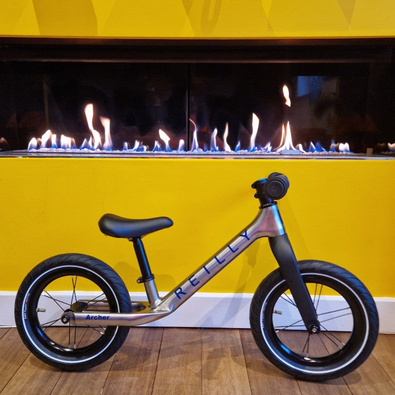 A titanium balance bike for children next to a fireplace
