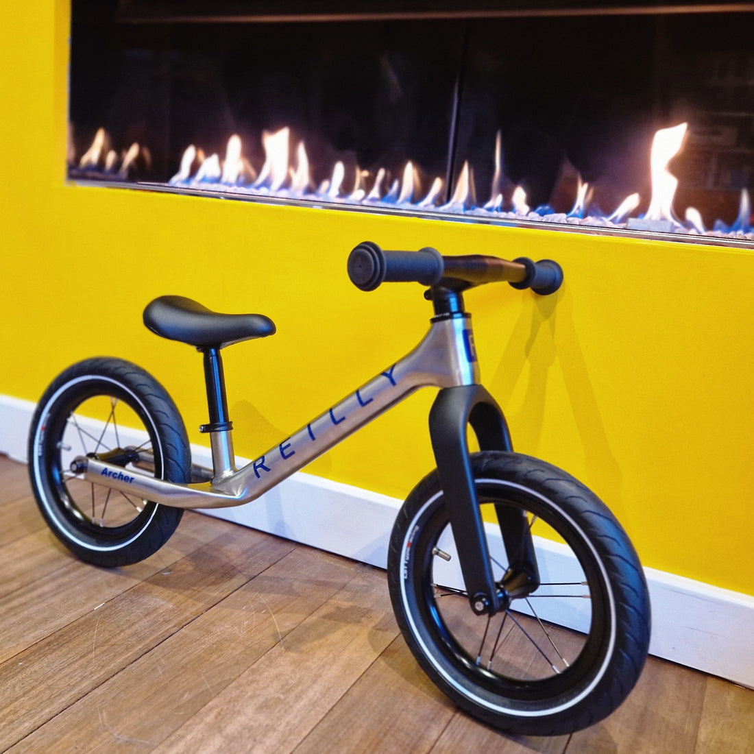 Children's balance bike in front of a yellow wall with a fireplace.