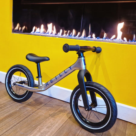 A titanium balance bike by a fire front view.
