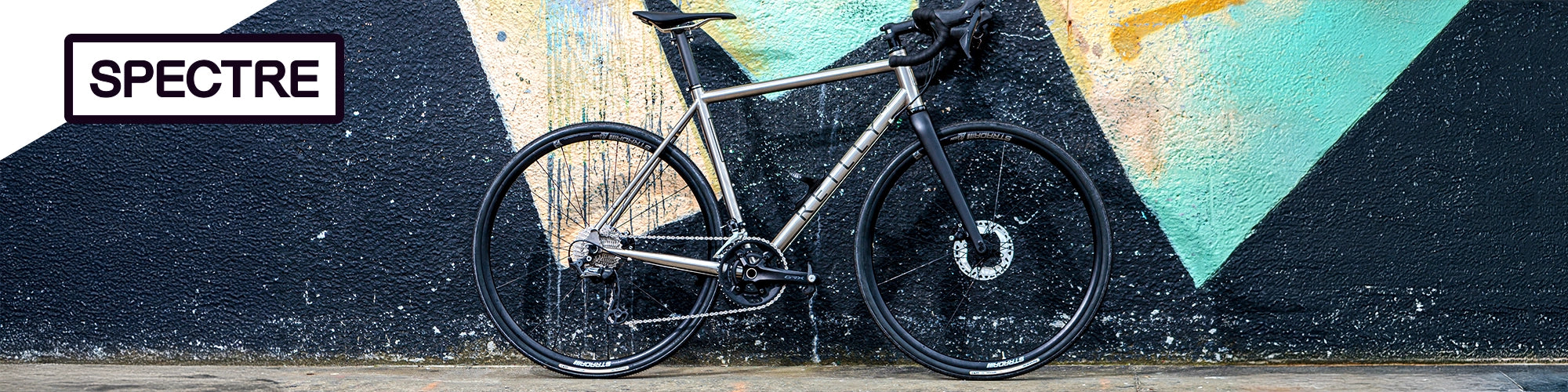 Titanium bicycle leaning against a wall with graffiti plus Pectre branding 