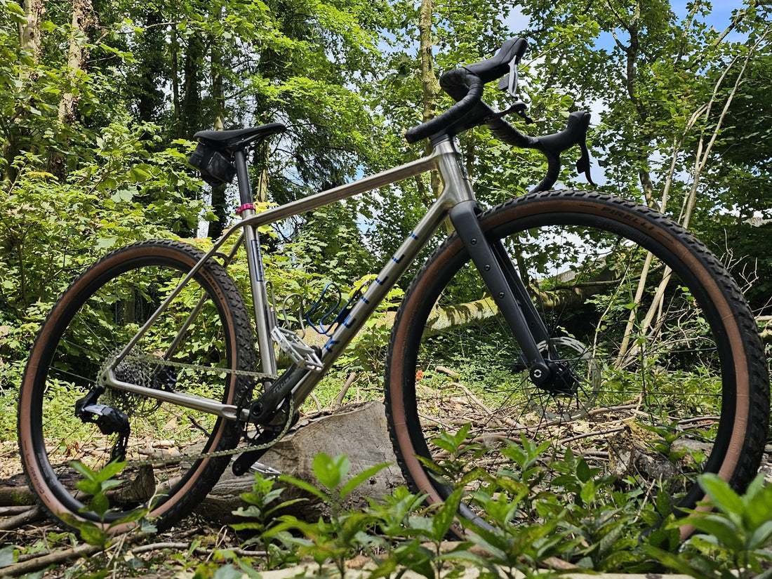 Titanium gravel bike in a forest setting with green trees and foliage.