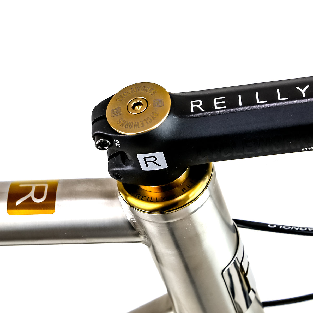 Close-up of a bicycle headset with a black Reilly stem, gold headset cup and collar, and a silver frame post on a white background.