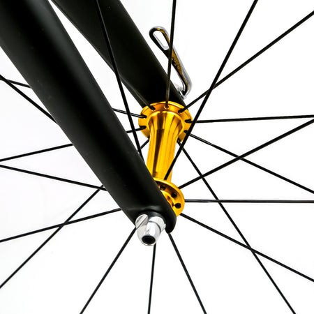 Close-up of a bicycle wheel hub with a shiny gold anodized finish, attached to a black fork with thin black spokes on a white background.
