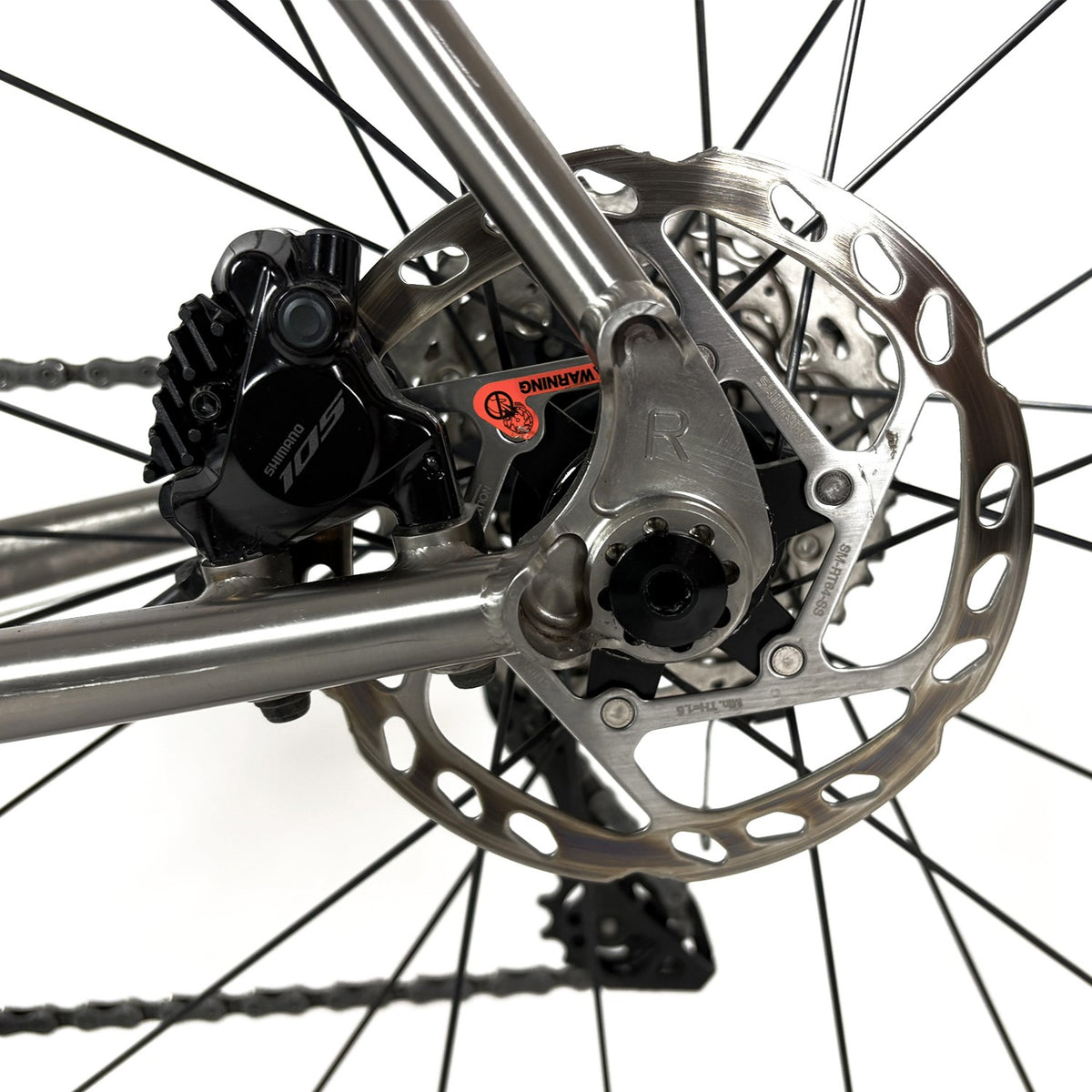 Close-up of a bicycle's rear disc brake assembly, featuring a silver metallic rotor, black brake caliper and Reilly branding.