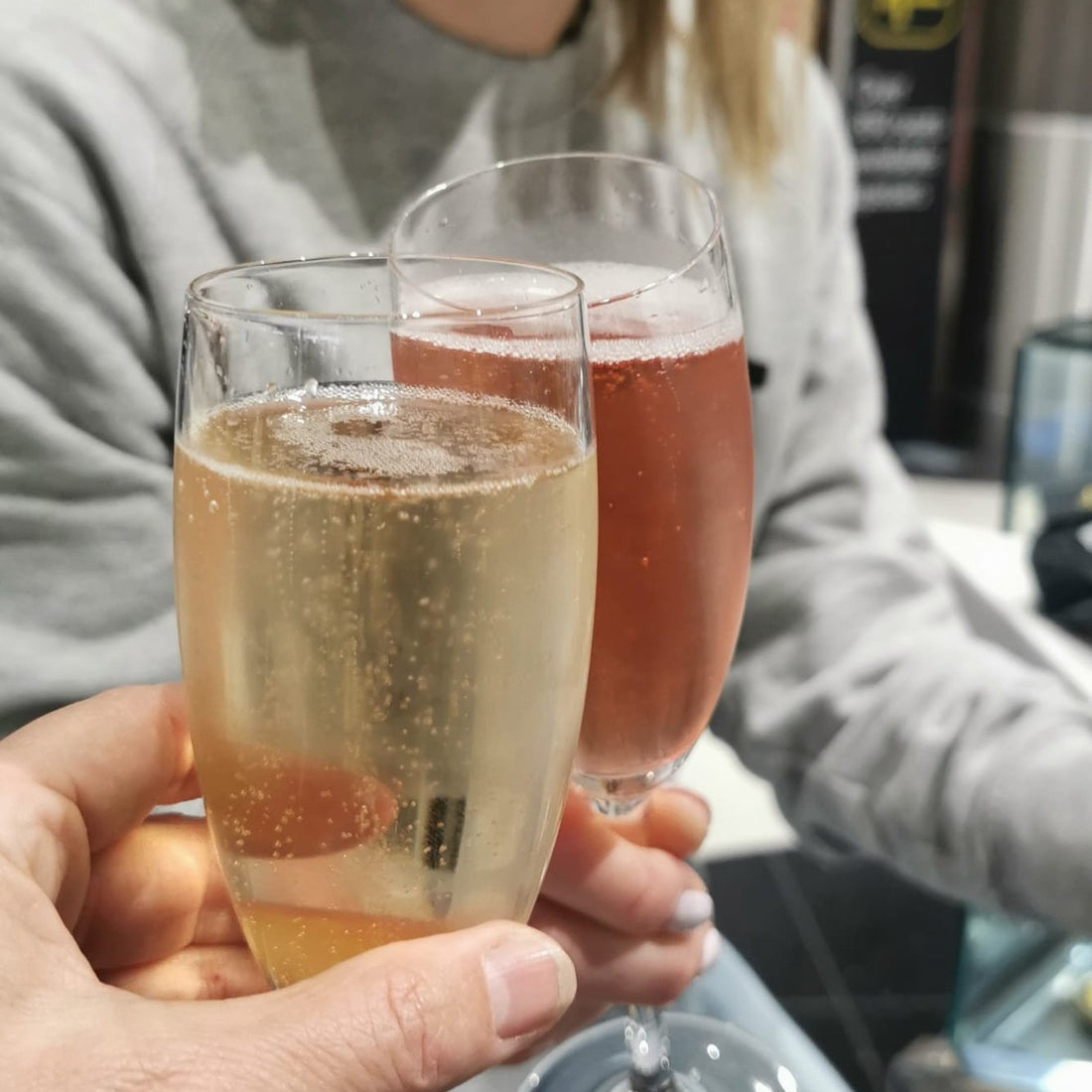 two glasses of wine, with one being held by a lady in a grey jumper.